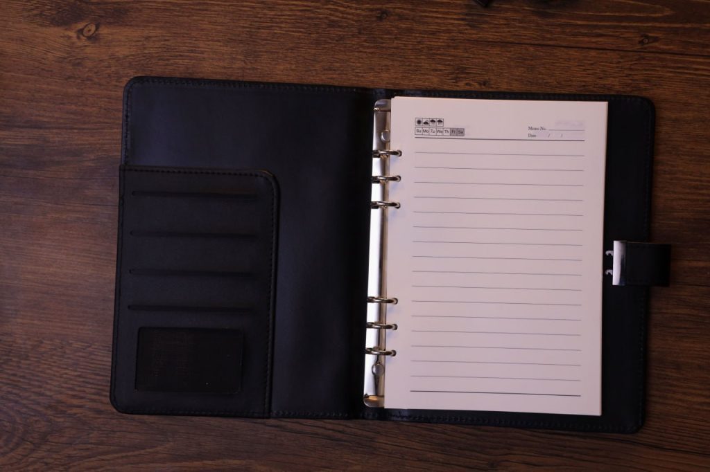 نوت بوك جلدي أسود مفتوح على مكتب خشبي، مثالي للتخطيط والهدايا الدعائية.