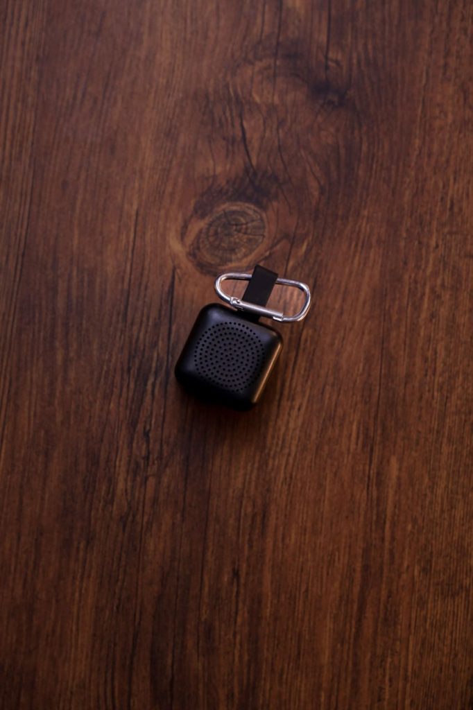 سماعة بلوتوث محمولة سوداء مع حلقة تعليق على سطح خشبي داكن.