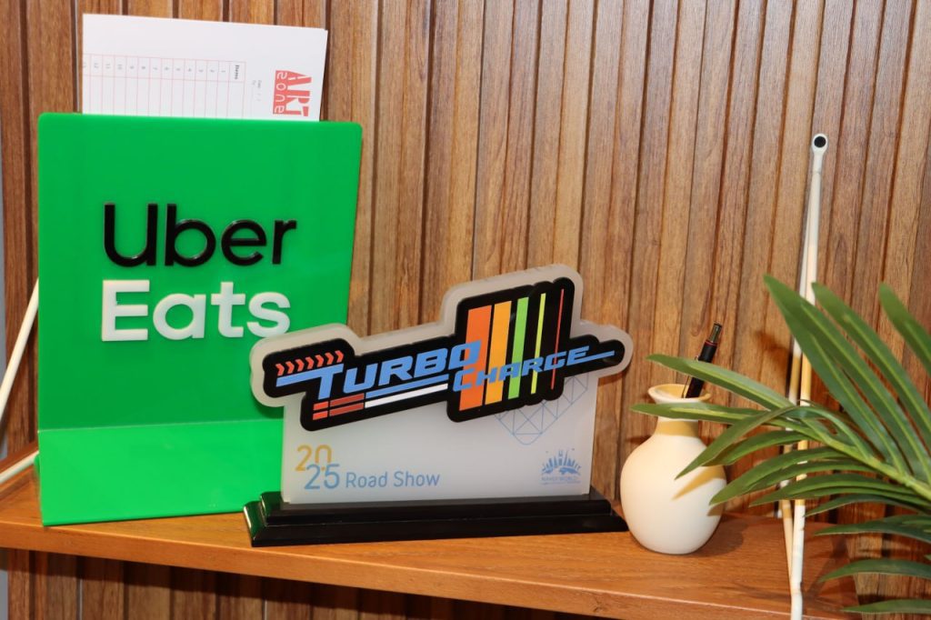 جائزة أكريليك "Turbo Charge 2025" ولافتة Uber Eats على رف خشبي هدايا دعائية.