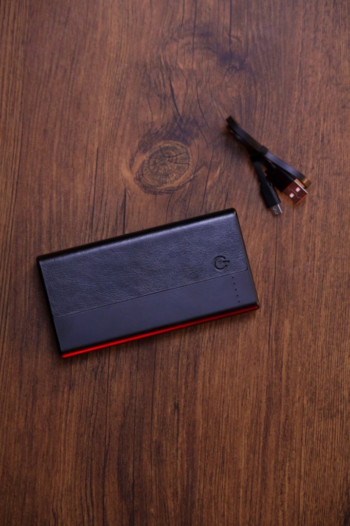 باور بانك أسود أنيق بشريط أحمر على سطح خشبي مع كابلات شحن.