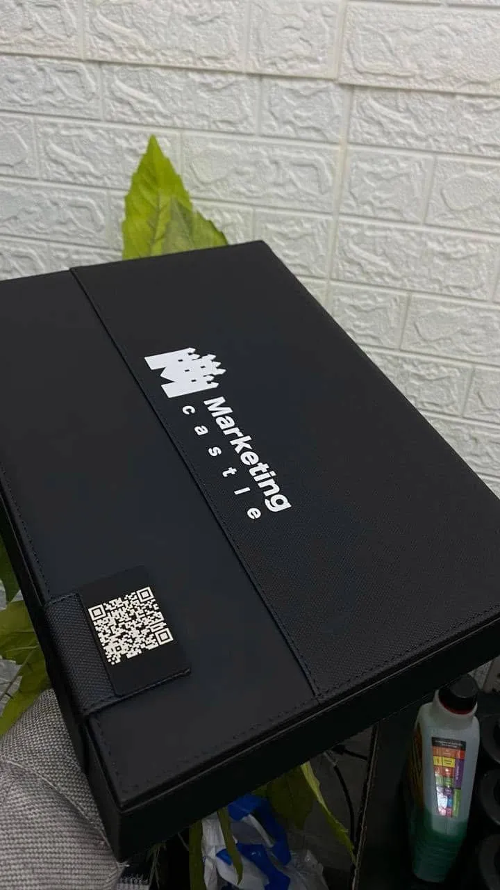 حافظة أعمال سوداء أنيقة تحمل شعار "Marketing Castle" ورمز QR على خلفية بيضاء.
