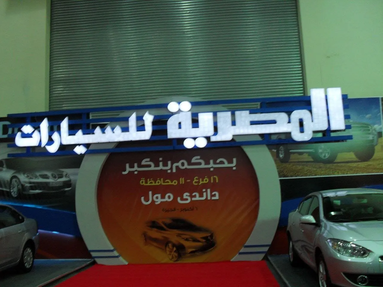 معرض المصرية للسيارات يعرض سيارات فضية ولافتات ترويجية ملونة.