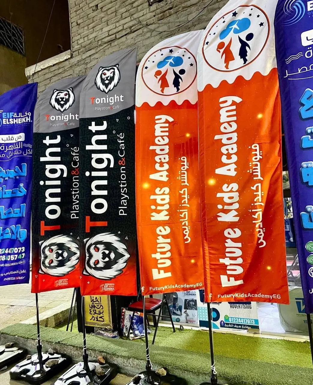 أعلام عمودية ترويجية لـ "Tonight Playstion & Café" و "Future Kids Academy" أمام مبنى.