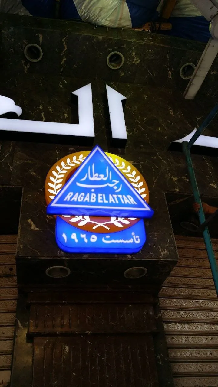 لافتة متجر "رجب العطار" المضيئة (تأسست 1965) باللون الأزرق والأبيض.