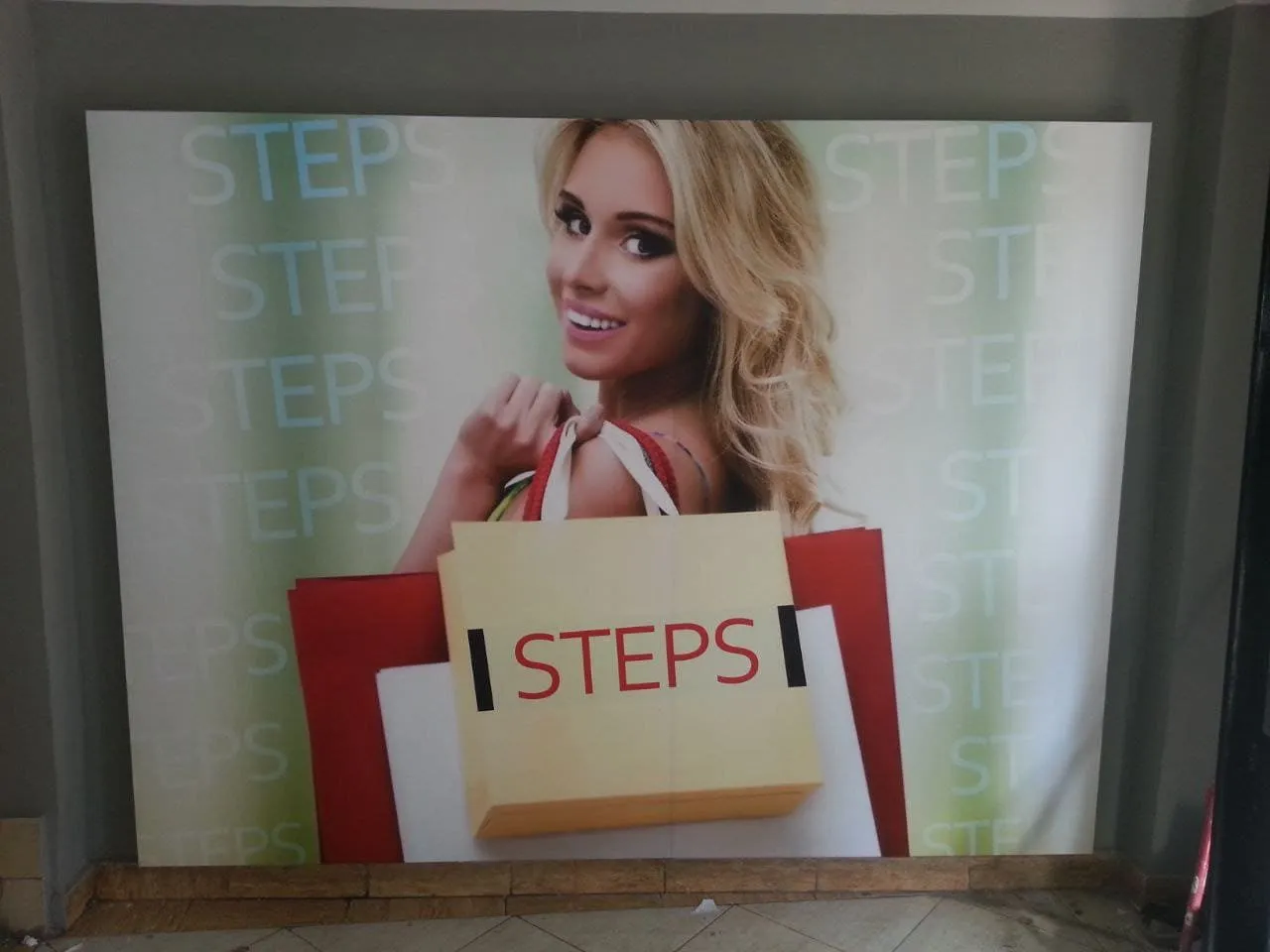 امرأة شقراء تحمل حقائب تسوق "STEPS" الملونة في إعلان ترويجي للتسوق.