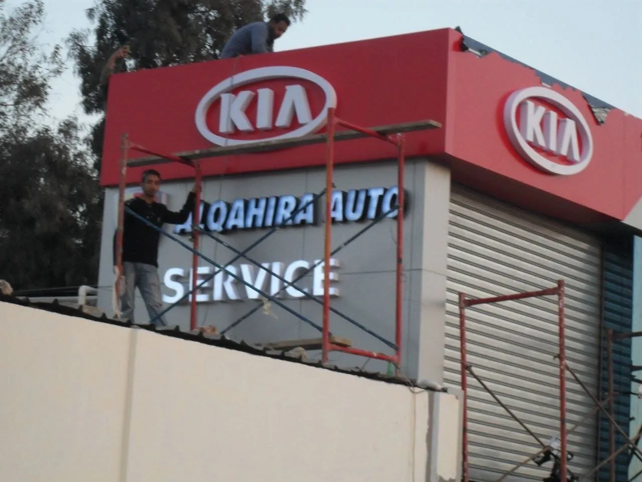 تركيب لافتة KIA وخدمات القاهرة للسيارات (ALQAHIRA AUTO SERVICE) على واجهة مبنى جديد.