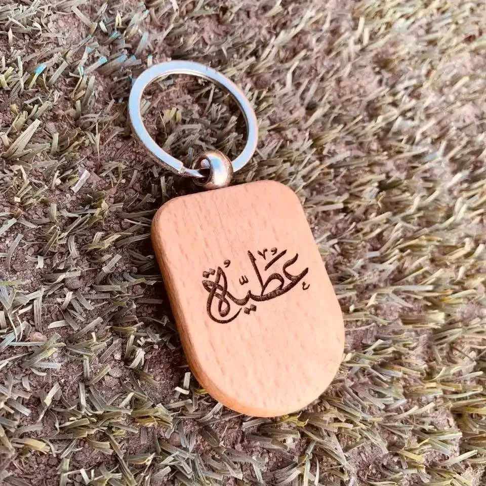 سلسلة مفاتيح خشبية محفورة بالليزر عليها اسم عربي مع حلقة مفاتيح معدنية.