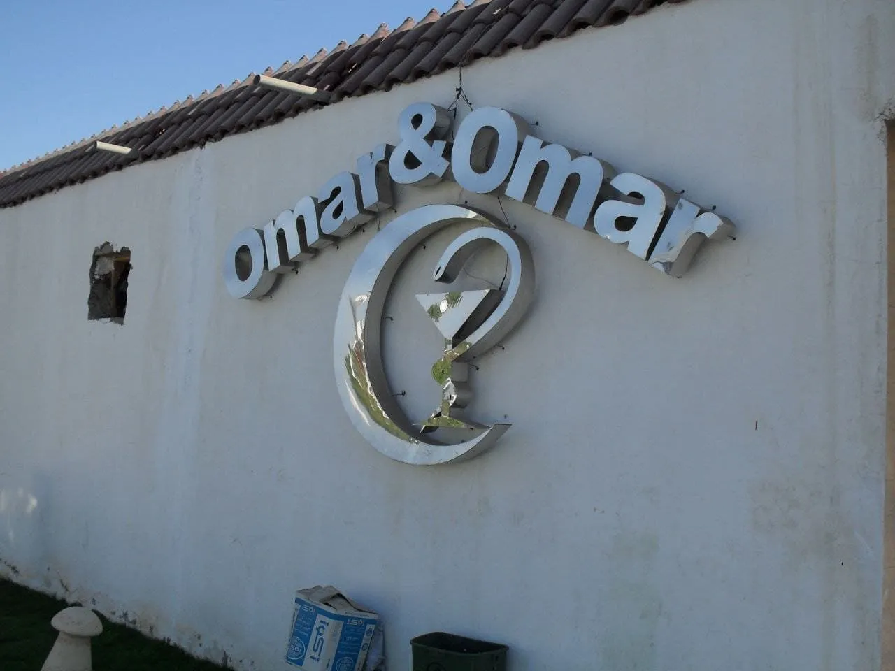 لافتة معدنية لامعة "Omar & Omar" بشعار هلال وكأس كوكتيل على جدار خارجي.