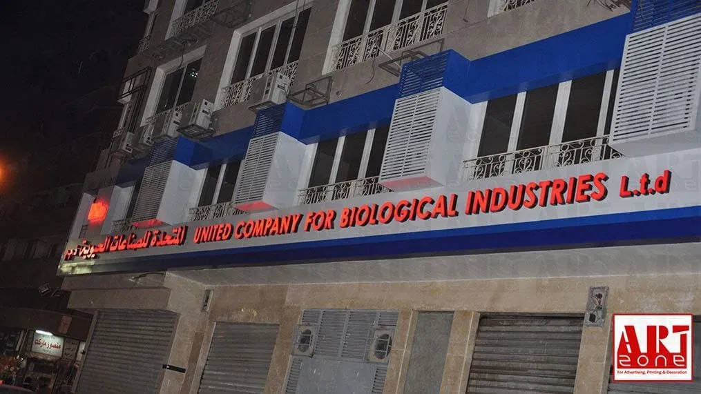 واجهة مبنى شركة الصناعات البيولوجية المتحدة (United Company for Biological Industries) ليلاً، لافتة مضيئة ضخمة.