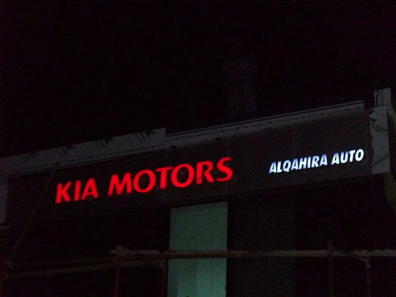 لافتة مضيئة لمركز "KIA MOTORS ALQAHIRA AUTO" ليلاً أثناء التركيب.