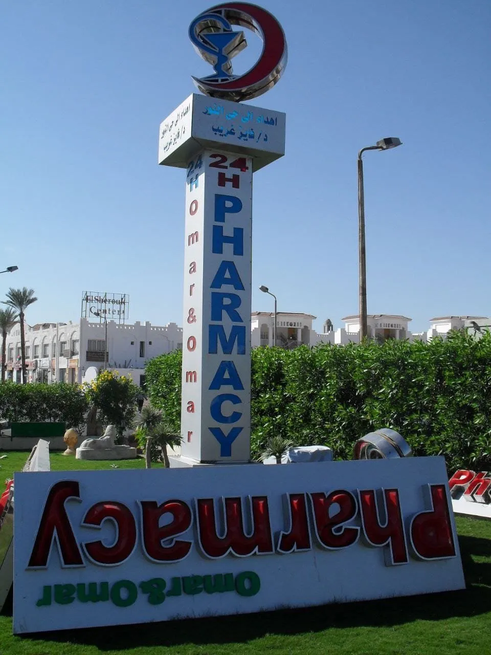 صيدلية عمر وعمر (Omar & Omar Pharmacy) بعمود إعلان طويل وشعار هلال أحمر على خلفية سماء زرقاء.