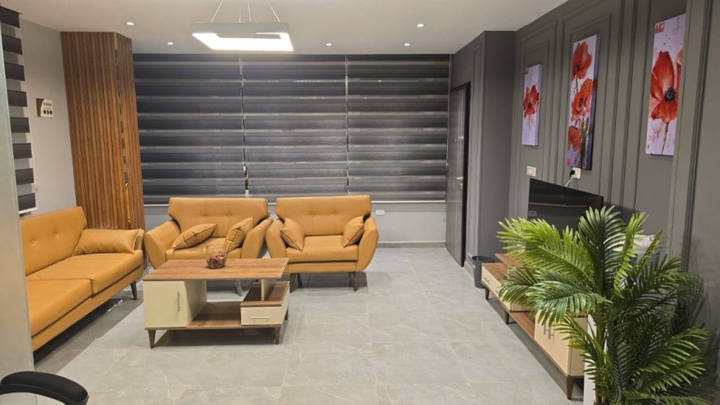 تصميم داخلي حديث لغرفة استقبال بمكتب، أثاث أصفر خردلي، لوحات خشخاش حمراء، وديكور رمادي.