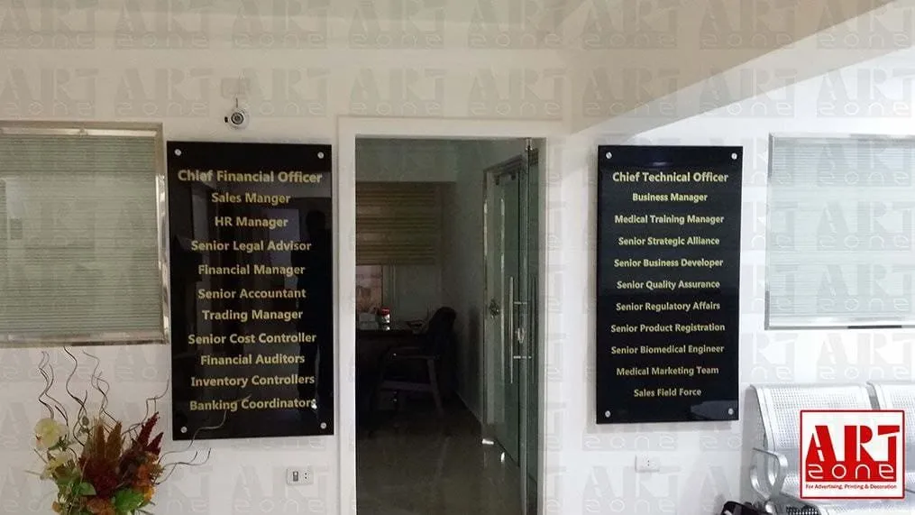 لوحات أسماء مناصب شركة مكتبيّة باللونين الأسود والذهبي بجوار مدخل داخلي.