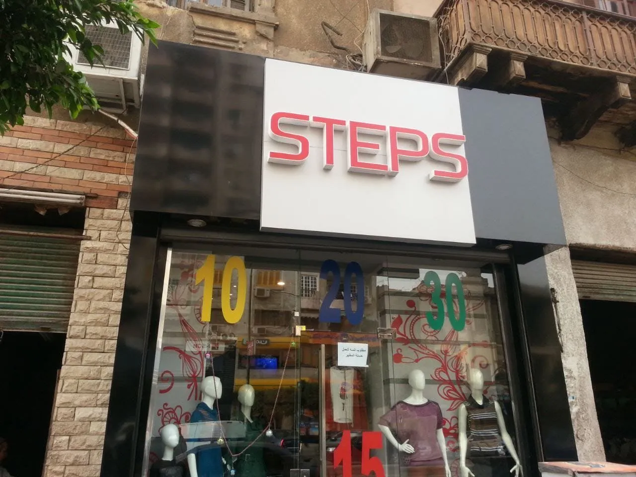 واجهة متجر ملابس "STEPS" بعرض تخفيضات وأرقام مشرقة على الزجاج.