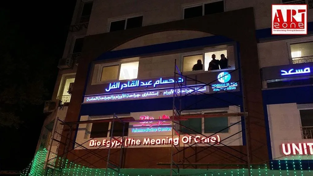 واجهة عيادة/مبنى طبي ليلاً بلافتات نيون مضيئة، تظهر سقالات وأضواء زينة خضراء.