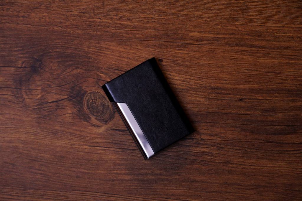 حافظة بطاقات عمل جلدية سوداء أنيقة مع لمسة معدنية على سطح خشبي داكن.