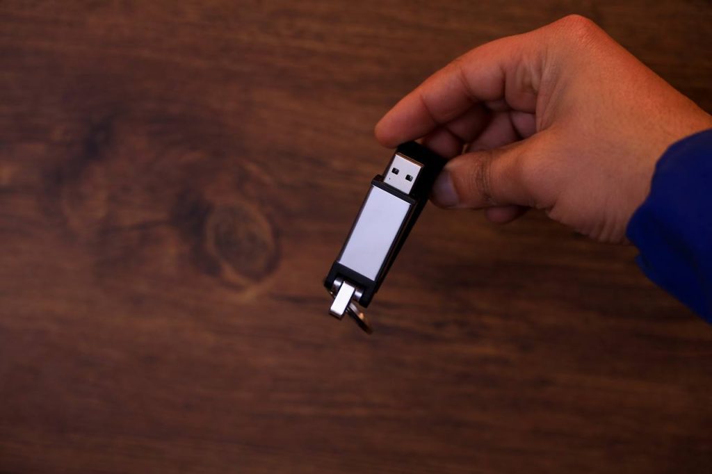 فلاشة USB سوداء وأنيقة تُمسك باليد على خلفية خشبية داكنة.